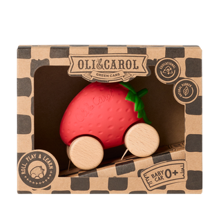 Oli & Carol Sweetie, la voiture pour bébé en forme de fraise, présentée dans un coffret cadeau en papier kraft, avec des badges en caoutchouc naturel, éducatifs et « roll-play-learn » (rouler, jouer, apprendre).