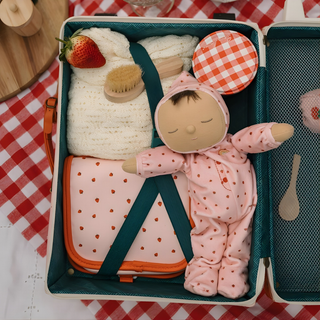 Olli Ella Dozy Dinkum Pip Strawberry, présentée dans une valise de voyage avec une couverture, une brosse et une pochette en forme de fraise ; poupée lestée aux yeux fermés, prête pour les aventures des vacances et les rituels du coucher