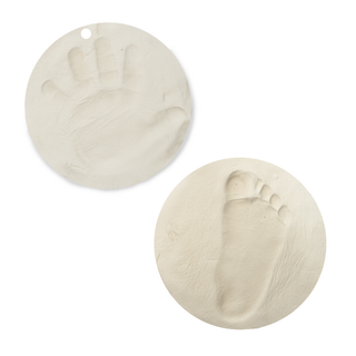 Two round white clay keepsake discs showing baby handprint and footprint impressions with hanging hole, Loolipo Patasec air-dry plant-based clay preserving tiny prints as lasting mementos