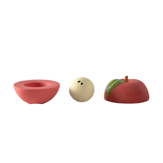Oli & Carol apple stacking toy with all three pieces displayed separately, two red half shells with stem and leaf detail and cream rattle ball
